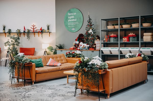 IKEA showroom lounge with leather sofas, green and red pillows, Christmas decorations, and shelving with storage baskets.