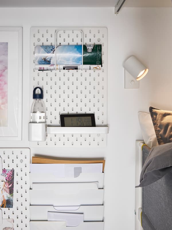 IKEA SKÅDIS pegboard mounted on a white wall next to a bed.