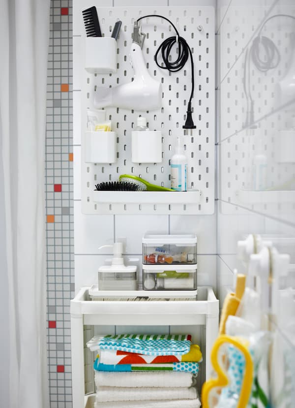 IKEA SKÅDIS small white pegboard and VESKEN white shelf unit work together to create a small bathroom storage center. Hang big gadgets and store boxes.
