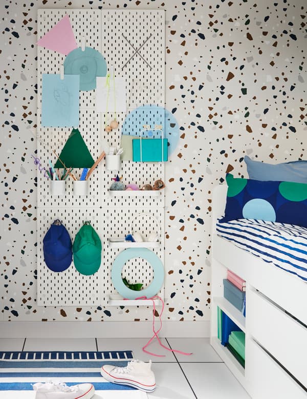IKEA SKÅDIS white pegboards beside a bed and used as a hanging bedside table, with white pegs, containers and mini shelves.
