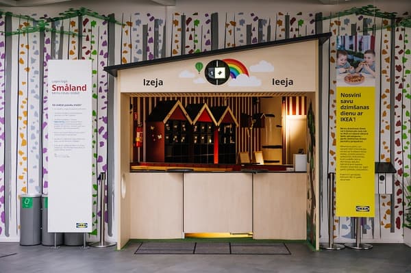 IKEA Småland rotaļu laukuma ieeja un izeja, kas veidota kā maza mājiņa ar varavīksnes zīmi, krāsainām meža tematikas sienas grafikām un informatīvām zīmēm latviešu valodā, kas aicina bērnus spēlēties un svinēt dzimšanas dienas.
