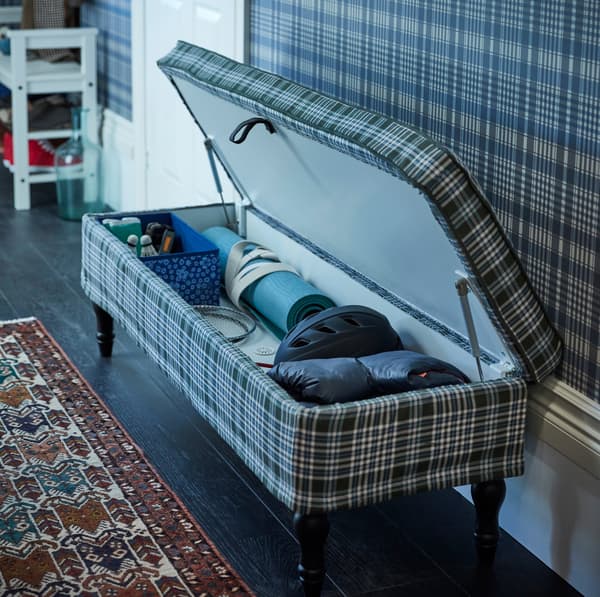 IKEA STOCKSUND blue, green and white plaid patterned long bench has dark wooden legs for a traditional feel and a closed storage compartment when lifted.