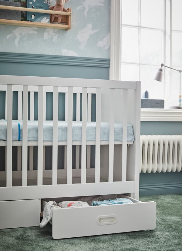 IKEA STUVA FRITIDS white cot in the high position. Lower white shelf is ajar holding baby blankets and bedsheets.