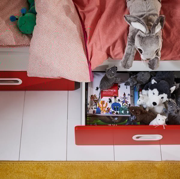 IKEA STUVA white cot with two drawers holding storybooks and stuffed animals.