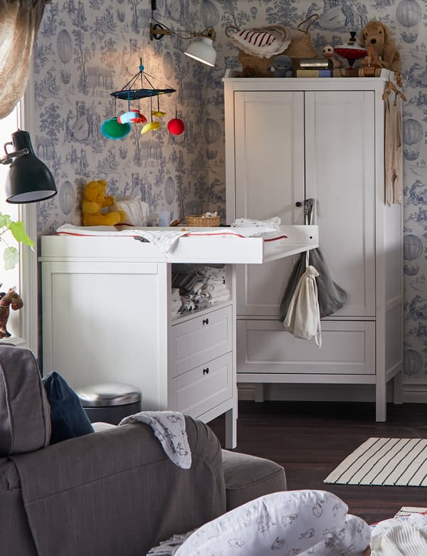 IKEA SUNDVIK changing table in a room with floral wallpaper, wardrobe, armchair, mobile and baby nursing items.