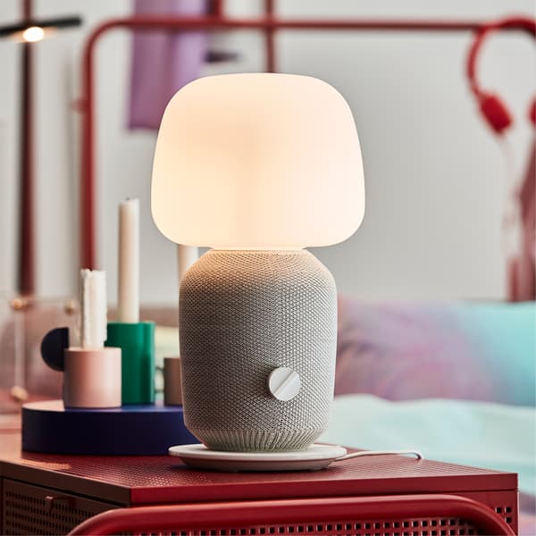 IKEA SYMFONISK stona lampa u beloj boji, na crvenoj komodi u spavaćoj sobi.