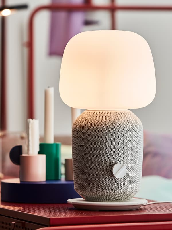 IKEA SYMFONISK table lamp in white that is standing on a red chest of drawers in a bedroom.