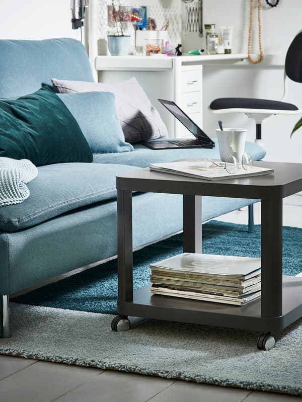 IKEA TINGBY dark brown side table on castors on a carpet next to a turquoise couch.