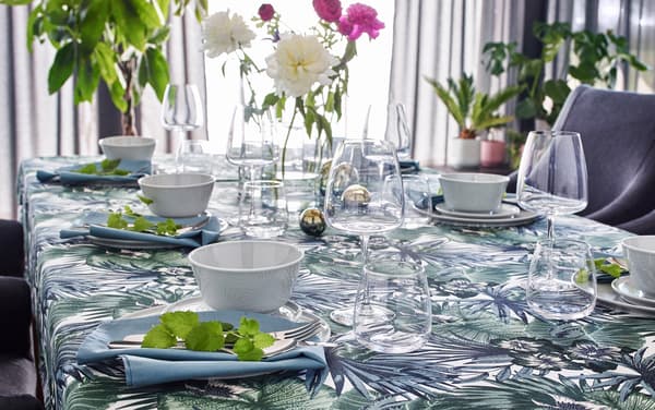 IKEA TORGERD fabric with a printed palm graphic pattern, laid on a dining table with clear glass CYLINDER vases and KRUSTAD white ceramic dishes.