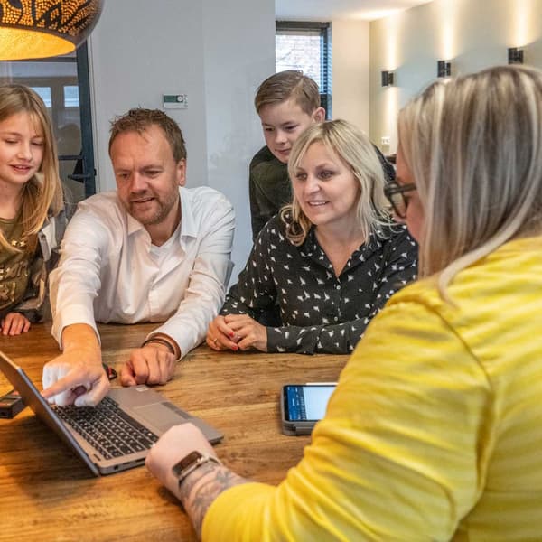 IKEA-työntekijä käymässä keittiösuunnitelmaa läpi asiakasperheen kotona ison puisen pöydän ääressä.