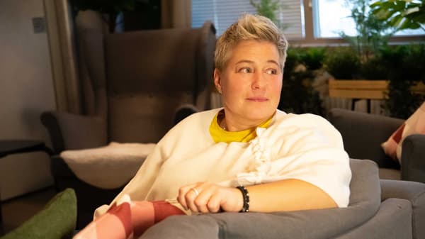 IKEA-työntekijän asuun pukeutunut henkilö istuu harmaalla sohvalla itse THORGUN-huovasta loihdittu viltti yllään.