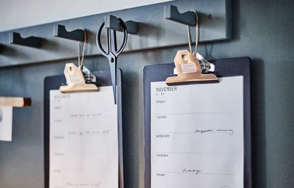 IKEA VÄLBEKANT clipboards hang from hooks on the wall, displaying a work schedule.