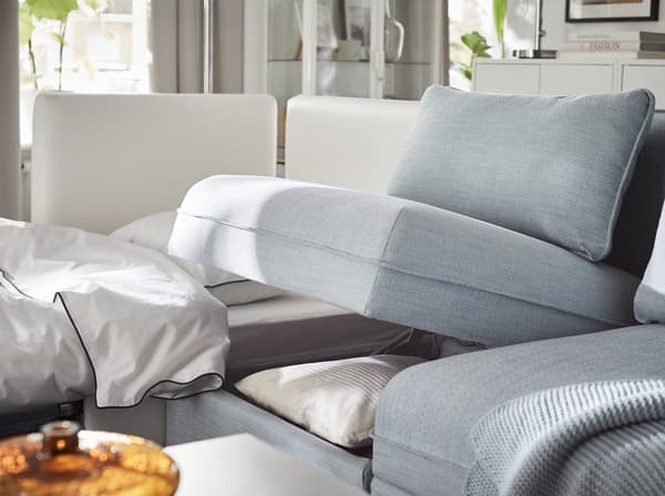 IKEA VALLENTUNA blue sofa unit with storage compartment propped open to reveal bedlinens and pillows.