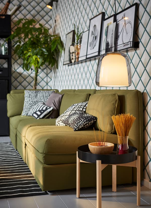 IKEA VALLENTUNA green modular sofa bed with storage, YPPERLIG birch and black coffee table and glass pendant lamp.