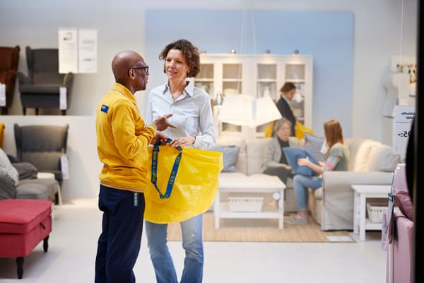 IKEA werknemer in bedrijfskleding helpt twee klanten in de winkel 
