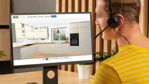 IKEA zaposlenik u žutoj majici razgovara s dvoje ljudi koji upotrebljavaju računalo za planiranje u odjelu kuhinja u robnoj kući.