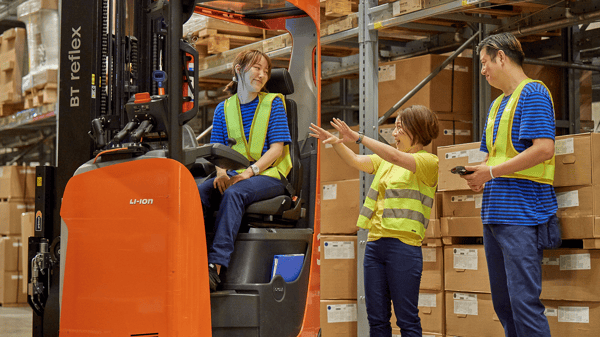 イケアのコワーカー3人が倉庫で話している。一人はフォークリフトに乗っている。