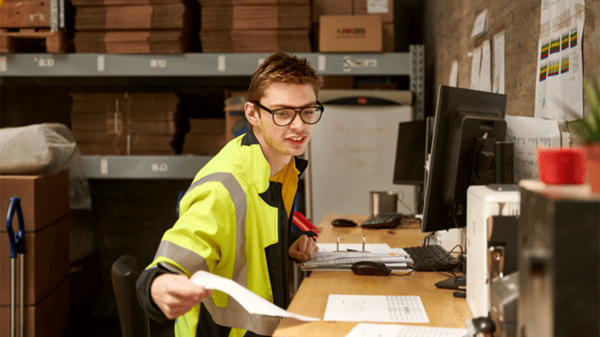 イケアのコワーカーが倉庫のパソコン前で書類を持って作業している