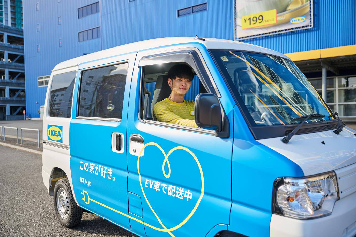 イケアのロゴ入り青いEV車に乗る人物。車体に『この車はEVです』『EV宅配実施中』の文字。背景にイケアの建物。