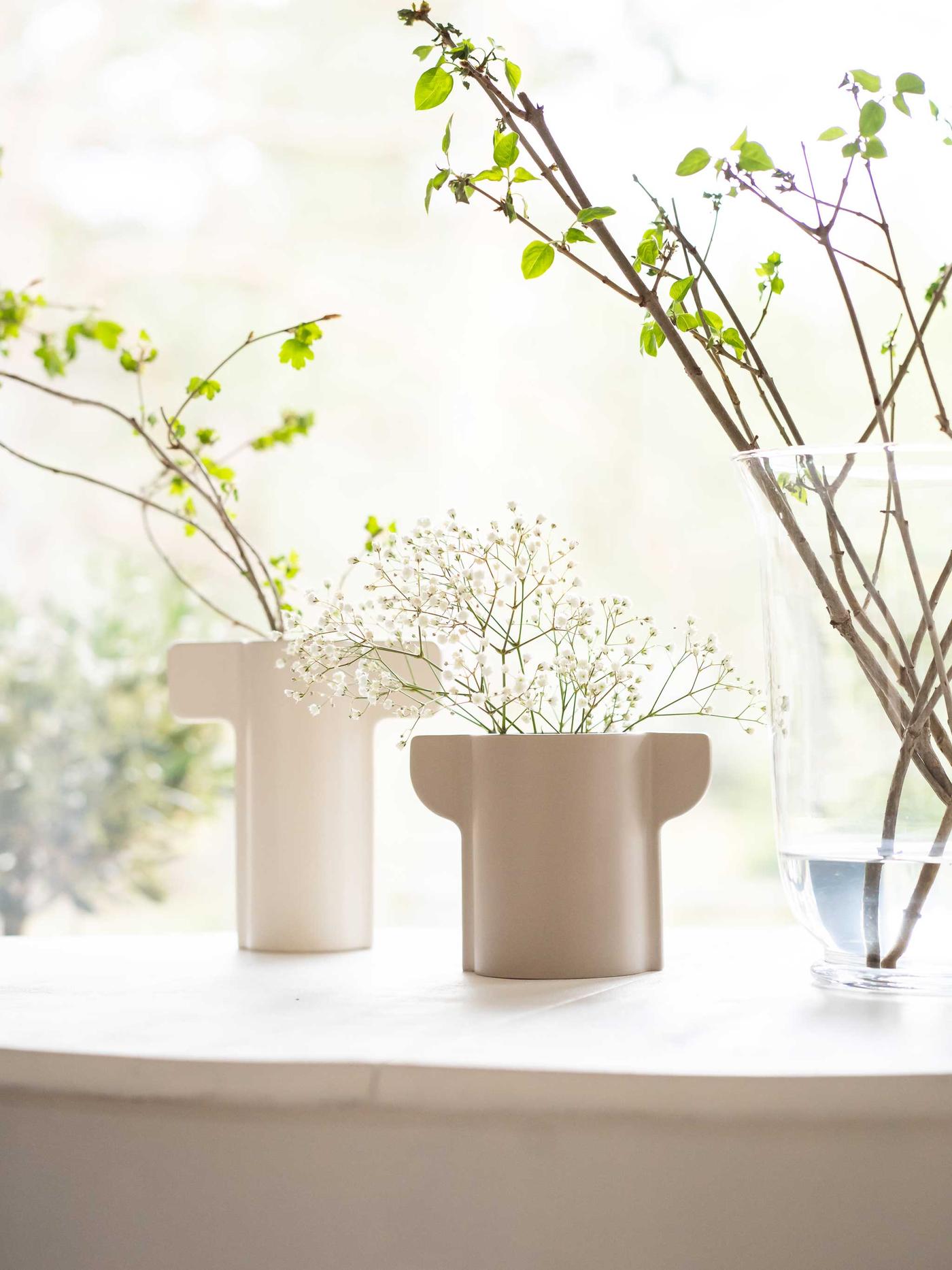 Ikkunalaudalla on kasveja ja vaaleansävyisiä maljakoita auringonvalossa.