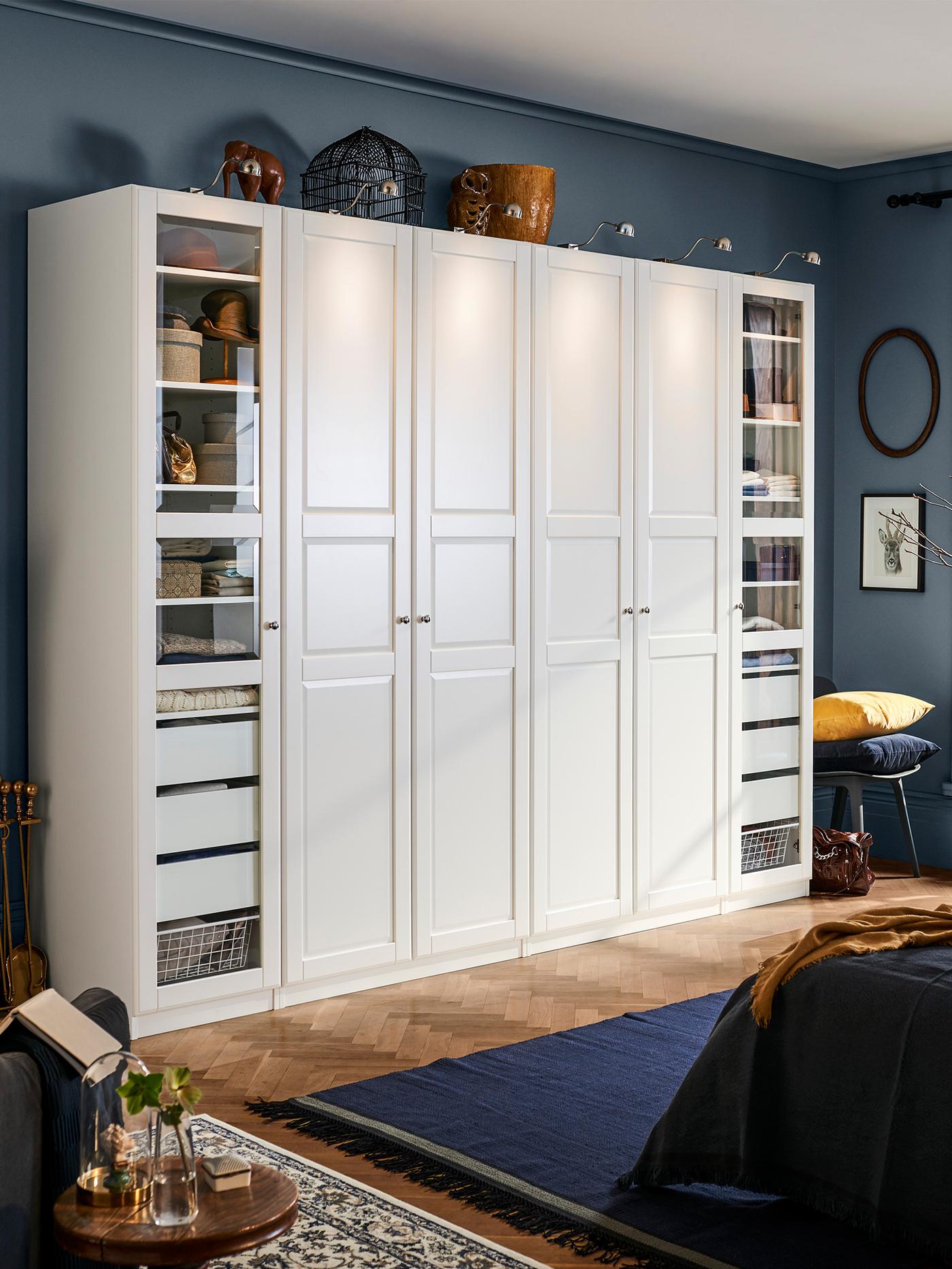 白いキャビネットが並ぶクローゼット。両側にガラス扉の棚があり、中央には引き出しと収納ボックスが配置されている。