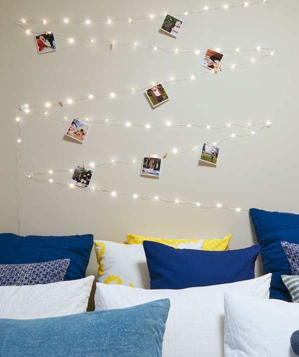 Illuminazione a LED per interni e foto appese alla parete sopra a un letto pieno di cuscini.