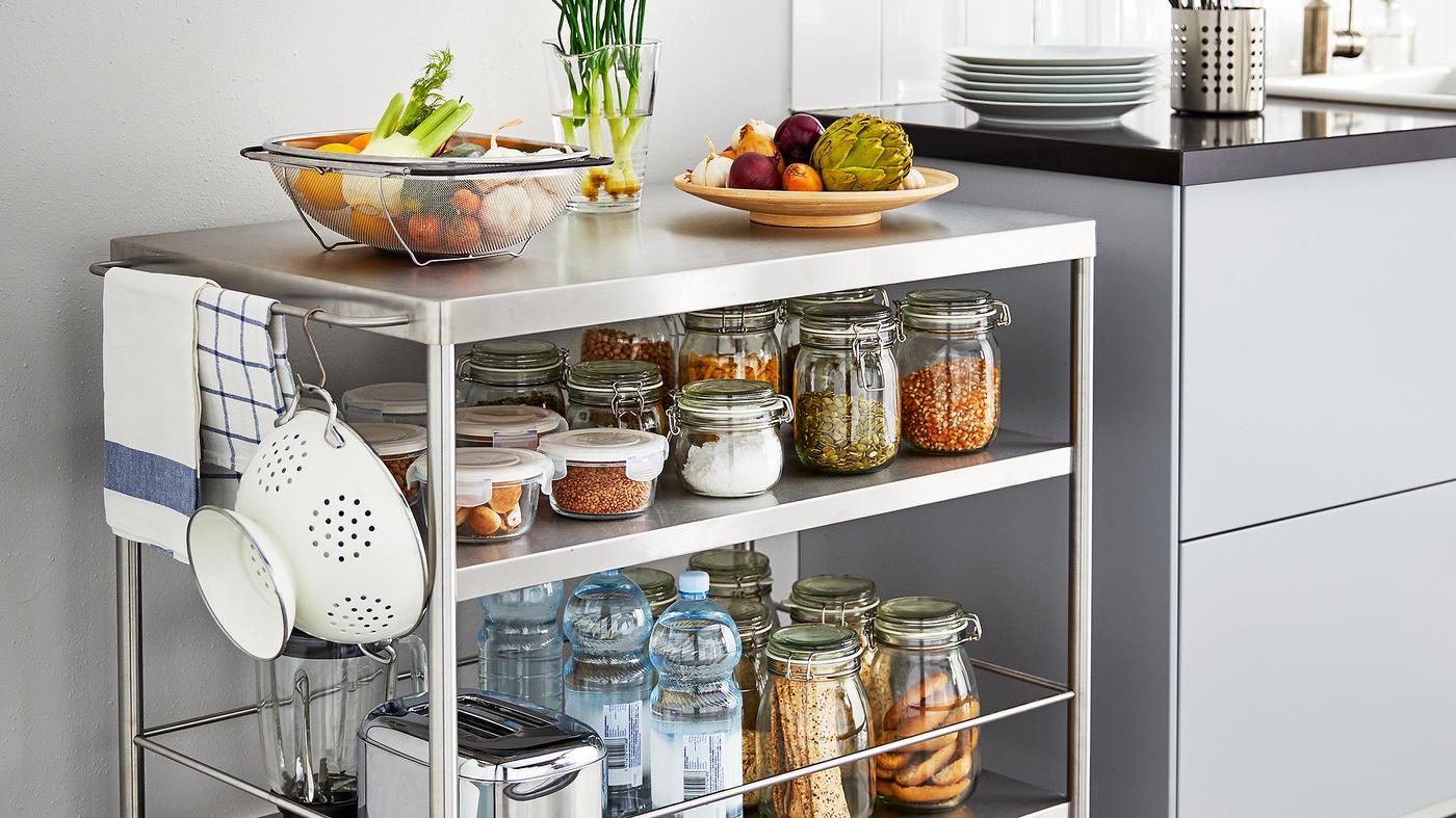 Îlot de cuisine métallique sur roulettes rempli de bocaux d’ingrédients, à côté d’un plan de travail.