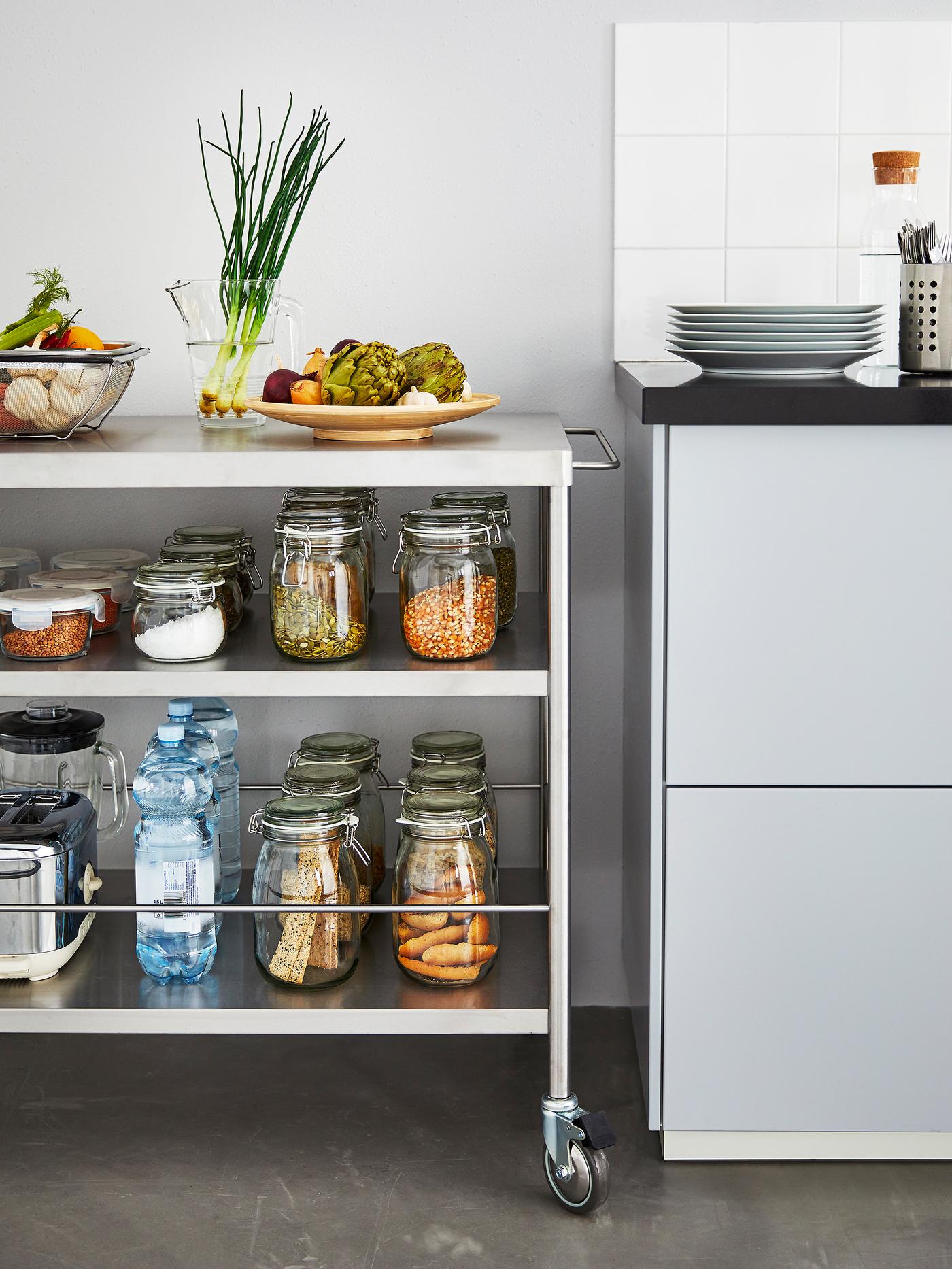 Îlot de cuisine métallique sur roulettes rempli de bocaux d’ingrédients, à côté d’un plan de travail.