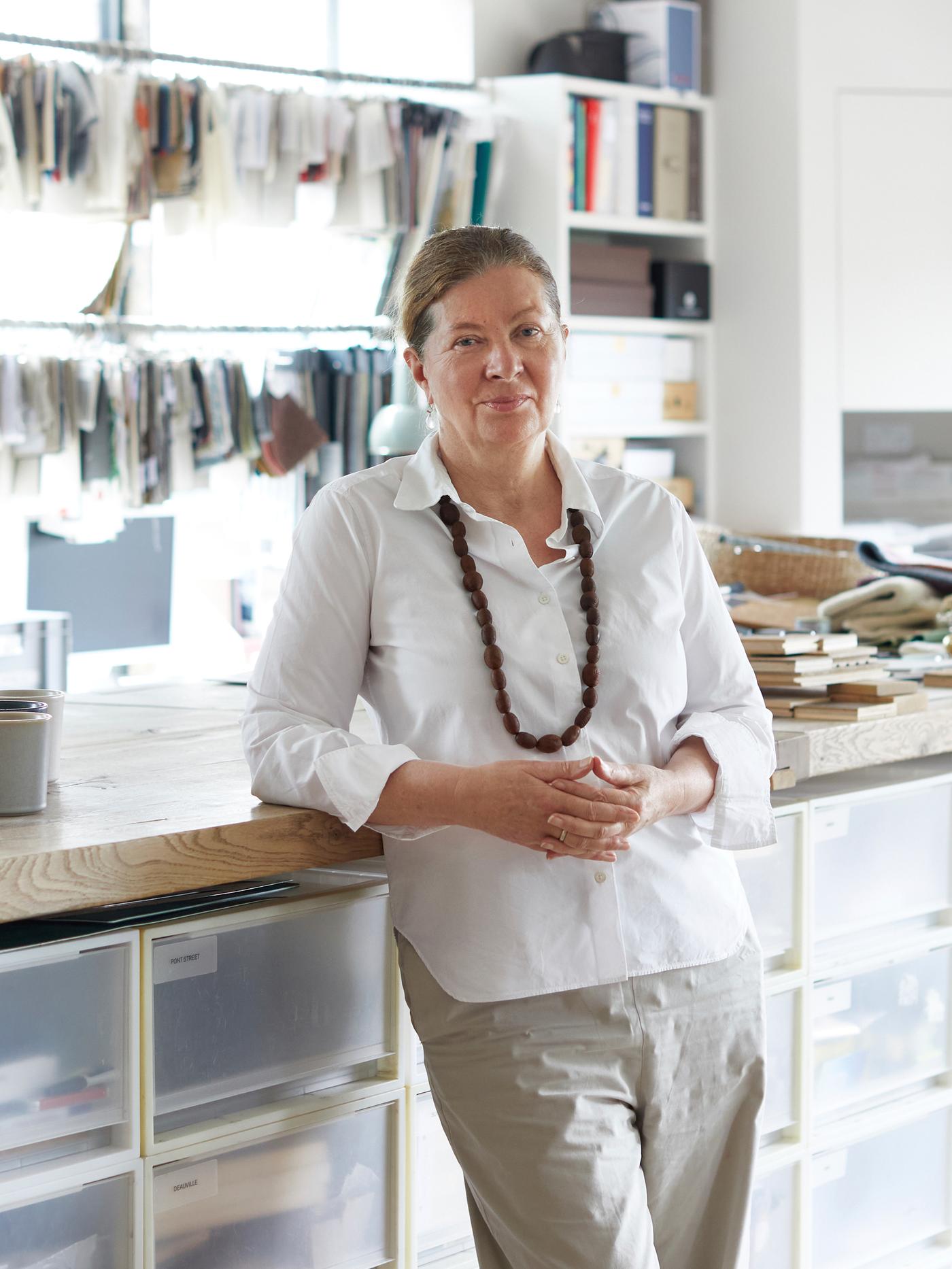 Ilse Crawford tervező fehér ingben, munkaasztalának támaszkodva, a stúdiójában.