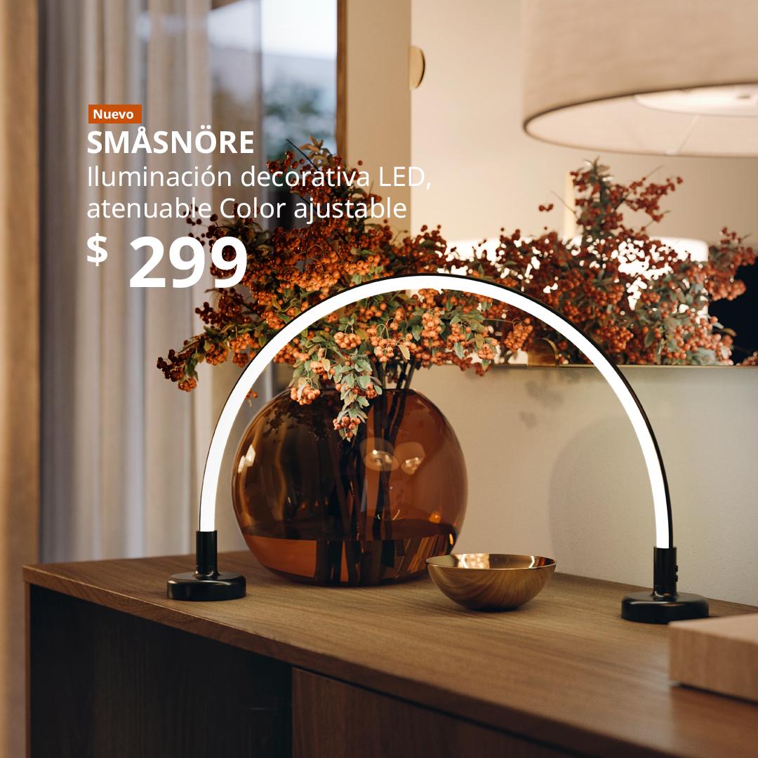 Iluminación decorativa LED SMÅSNÖRE y un florero STOCKHOLM 2025 con flores, colocados sobre un gabinete junto a una ventana.