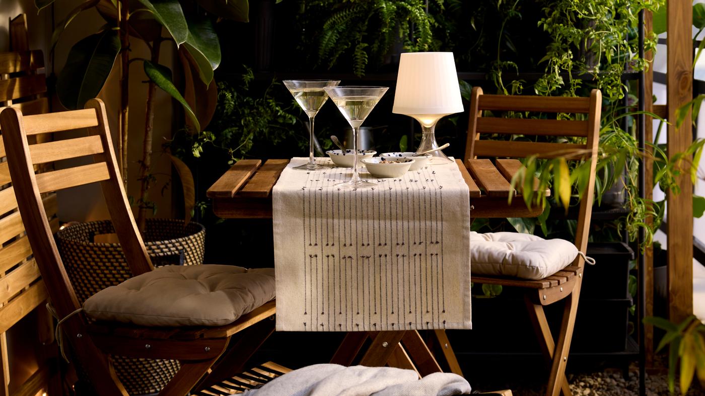 Im Außenbereich sind Sommermöbel aufgebaut mit einem Tisch, zwei Stühlen und zwei Sektgläsern.