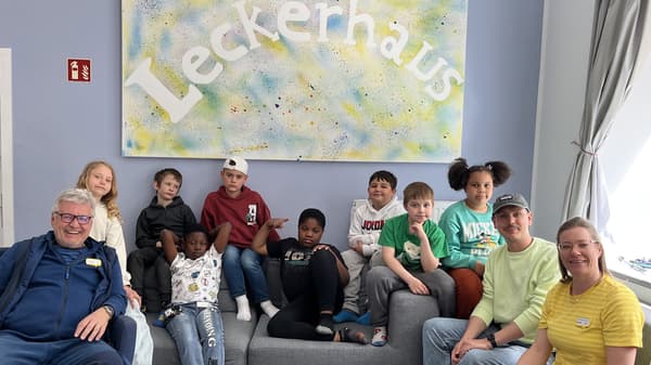 Im Hintergrund an der Wand hängt ein großes buntes Bild mit dem Schriftzug 