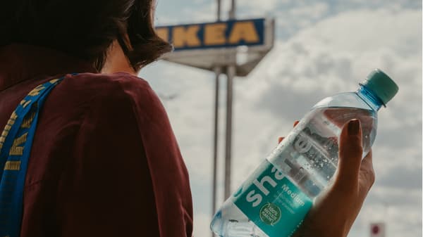 Im Hintergrund ist das IKEA Logo zu sehen und im Vordergrund wird eine Wasserflasche von share gehalten.