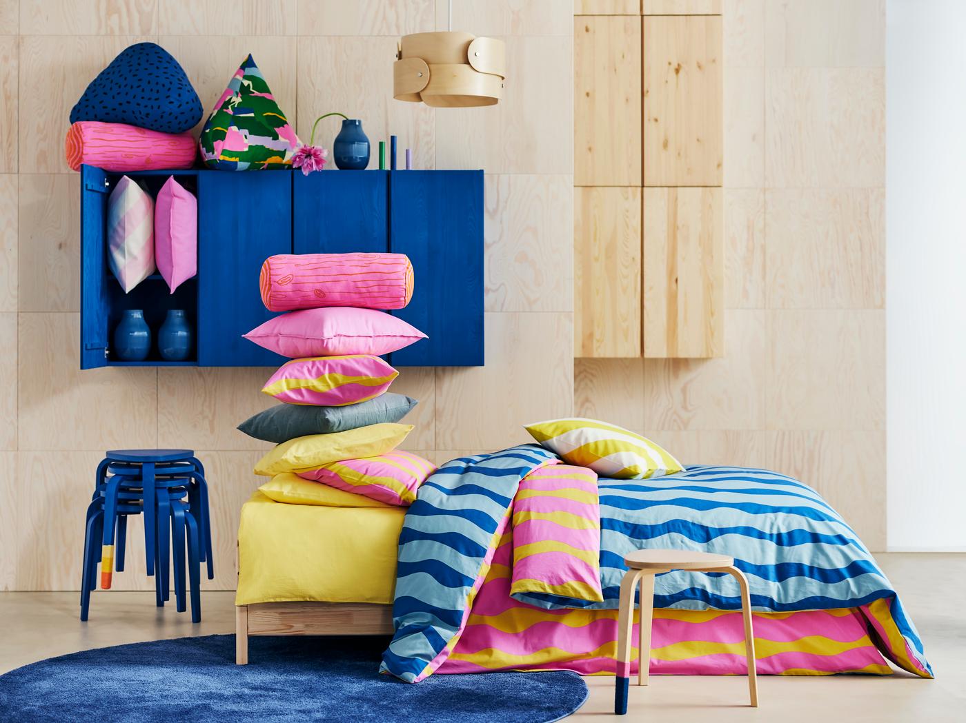 Image of a bedroom with IKEA's new bright blue, pink and yellow bedding beside blue and natural wood cupboards.