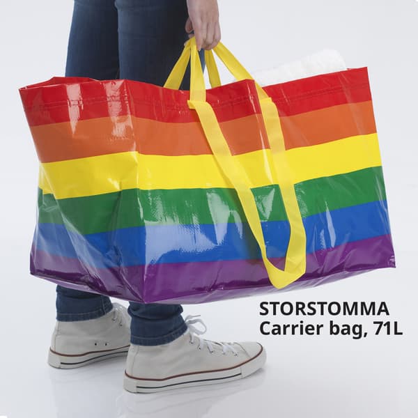 Image of a hand holding a large STORSTOMMA carrier bag, 71 litres, with colourful strips. 