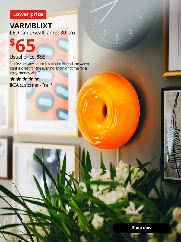 Image of a orange glass VARMBLIXT LED table/wall lamp hung on a wall decorated with art decoration displayed using RODALM. A “Lower price" tag appears on the image. Text reads: “VARMBLIXT, LED table/wall lamp, 30cm, $65. Previous price slashed $85.” Rated 5 stars by IKEA customer Tra**. "It elevates any space it is placed in, and the warm light is great for the evening and night time for a cosy, moody vibe.”