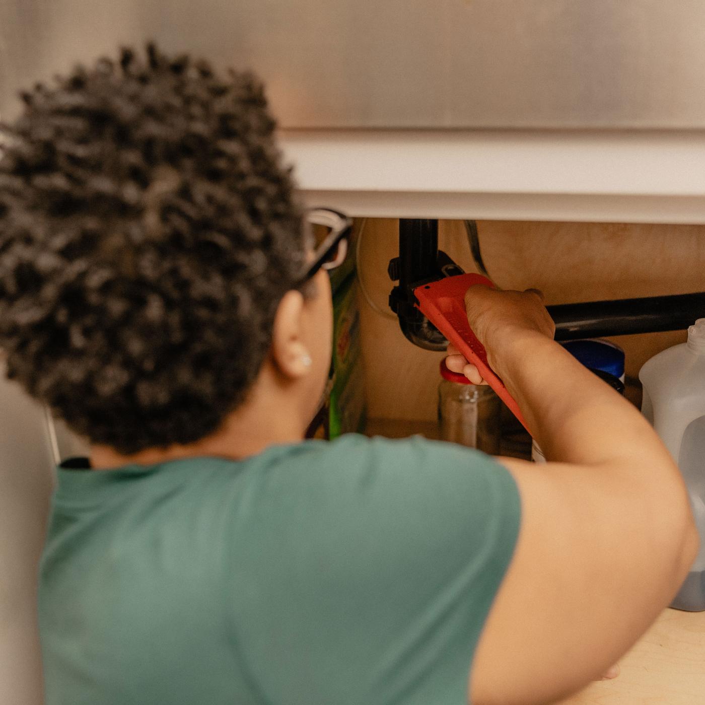 Image of a plumber tightening a pipe under the sink in the cabinet