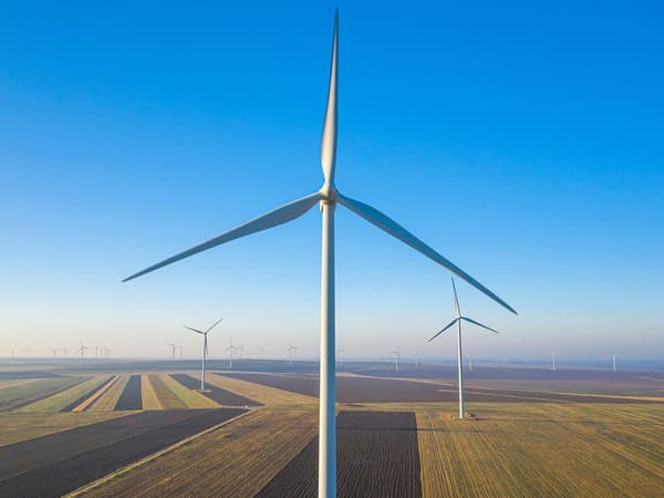 Image of a wind turbine with more turbines behind it in a green field with a blue sky in the background.