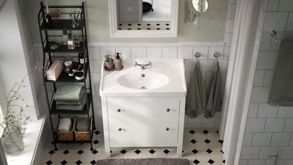 Imagen de baño desde arriba, donde hay un lavamanos blanco junto a mueble estante negro con productos de baño.