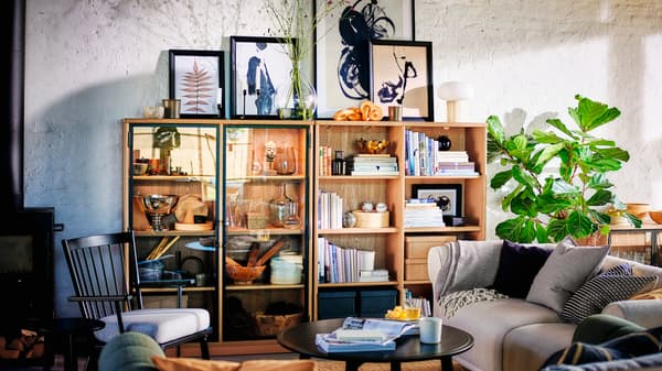 Imagen de una sala con un estante de madera con libros y decoración junto a sofá gris.