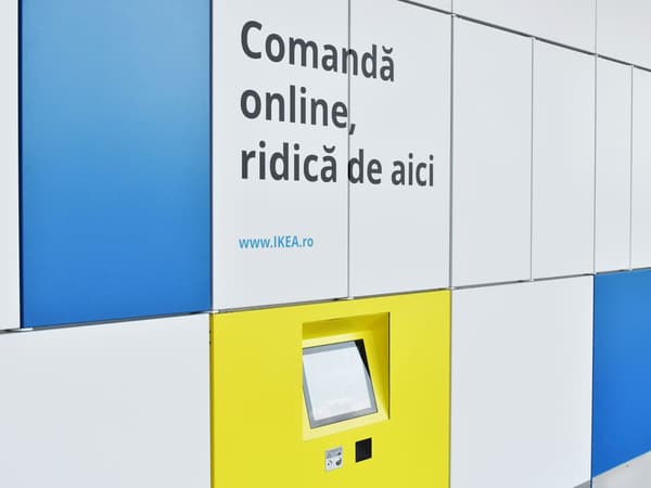 Imaginea arată un perete cu panouri albastre, albe și galbene. Pe panoul alb este scris textul "Comandă online, ridică de aici" și adresa web "www.IKEA.ro". În panoul galben există un ecran tactil pentru ridicarea comenzilor online.