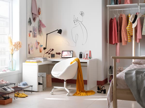 Imatge d’una habitació juvenil, decorada amb tons rosa pastel i blanc, amb un bonic escriptori, un llit de fusta clara i un armari obert. Sobre la paret, hi destaca un dibuix d’una dona al costat d’un tauler perforat. La llum entra per la finestra i fa que l’aspecte sigui molt acollidor.