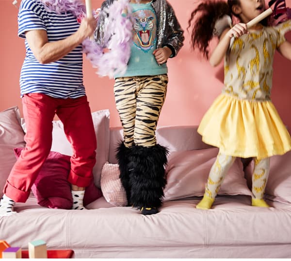 Imaxe recortada onde se ven as pernas de tres nenos xogando xuntos sobre un sofá rosa.