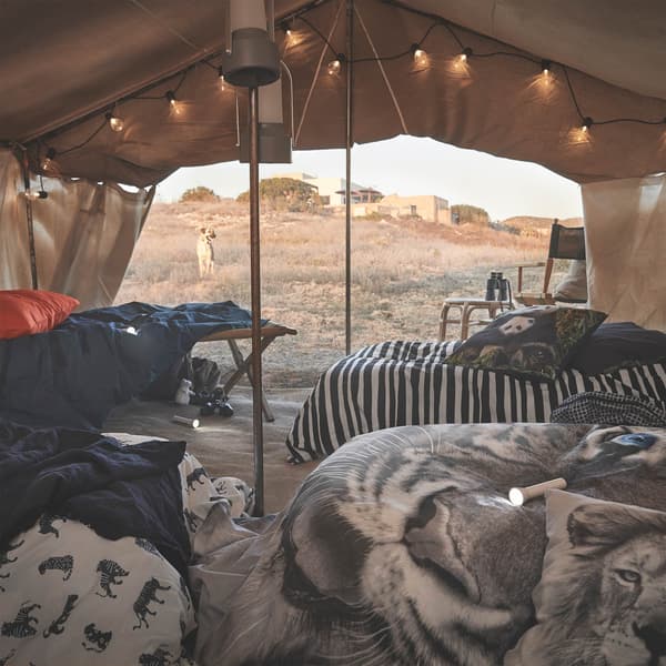 Immagine di una tenda con lucine decorative e copripiumini URSKOG con stampe ispirate ad animali selvatici. Ci sono anche un paio di torce.