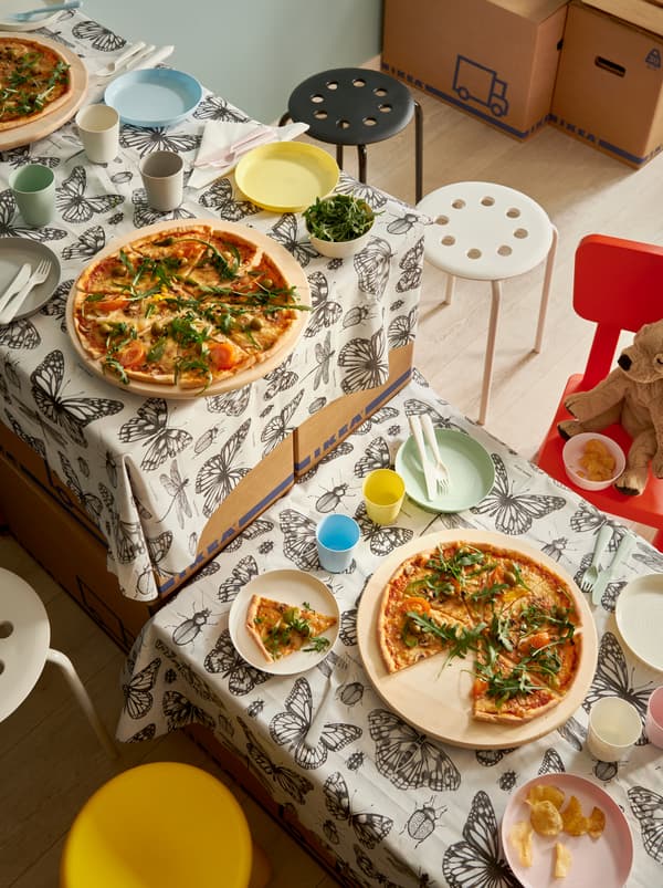Improviseret bord af flyttekasser med SOMMARMALVA badeforhæng som duge, dækket med pizza på SNUDDA drejebakker.