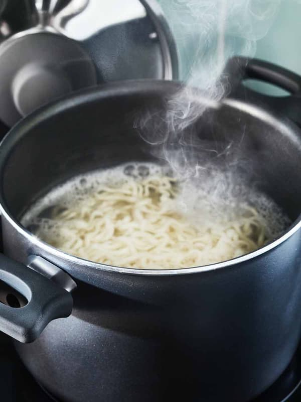 In a black pot, pasta is cooking on a stovetop.