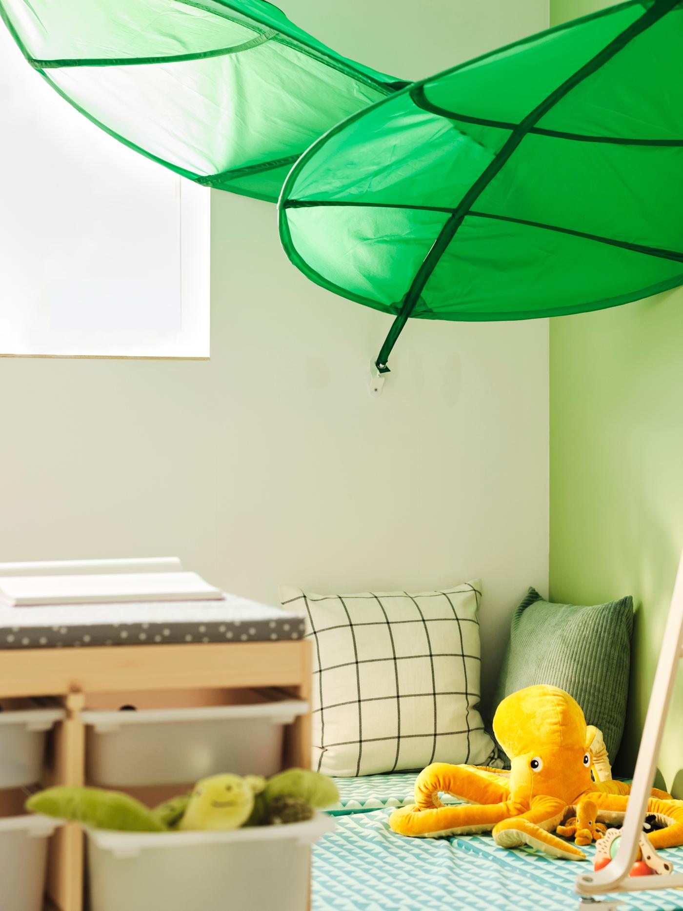 In a cosy corner, a parent sits underneath several LÖVA leaf canopies with a small child and two babies.