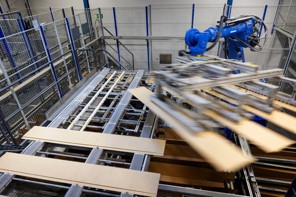 In a factory setting, a blue robotic arm lifts three sides of a BILLY bookcase.