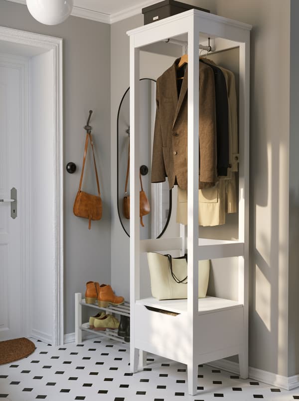 In a hallway with a black-and-white-patterned floor stands a white IDANÄS open wardrobe, a few jackets on hangers in it.