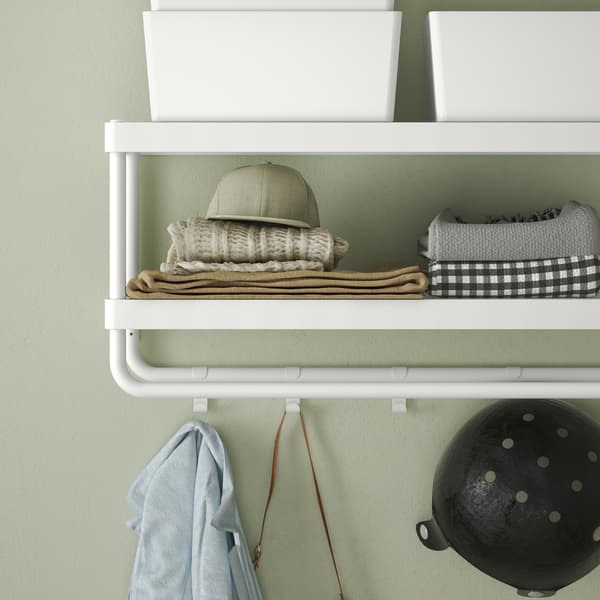 In a hallway with light green walls hangs a white hat rack with shelves and hooks for scarves, boxes and gloves.